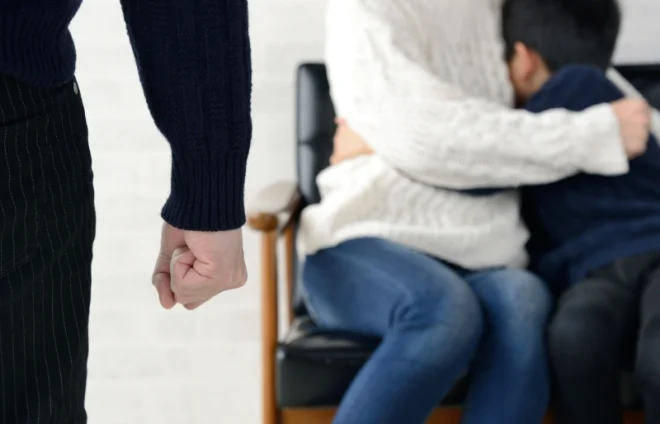 Clenched fist in foreground as parent comforts child on couch, highlighting divorce conflict risk inside