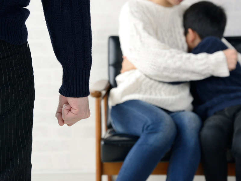 Clenched fist in foreground as parent comforts child on couch, highlighting divorce conflict risk inside