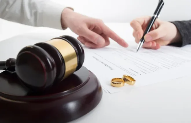 Gavel, rings, and lawyer guiding client signing divorce agreement paperwork on white desk in office