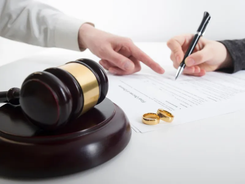Gavel, rings, and lawyer guiding client signing divorce agreement paperwork on white desk in office