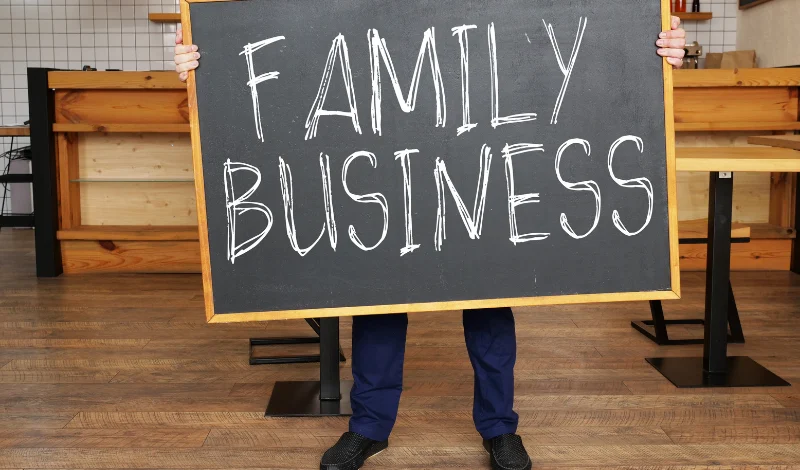 Person holds chalkboard reading Family Business in cafe, discussing divorce impacts on shared company today