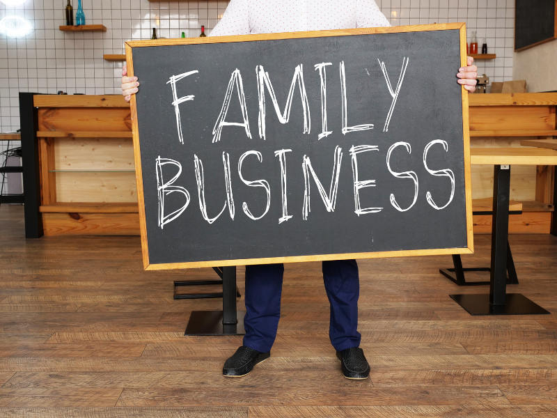 Person holds chalkboard reading Family Business in cafe, discussing divorce impacts on shared company today