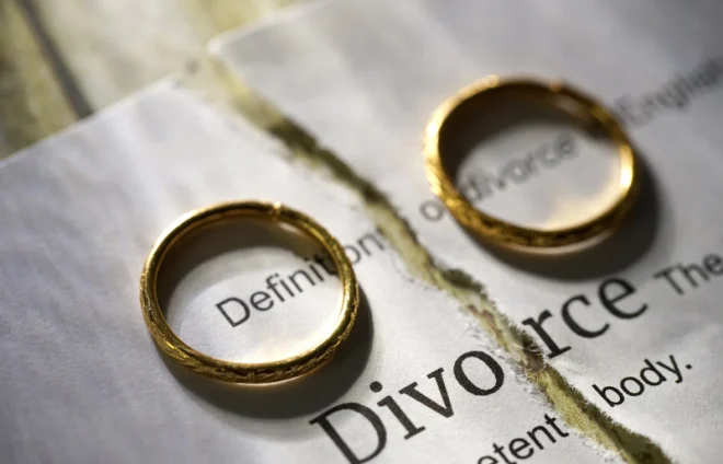 Two gold rings rest on torn divorce document, symbolizing separation, legal proceedings, and heartbreak ahead