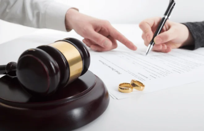 Gavel and wedding rings beside document as person signs divorce agreement under legal guidance today