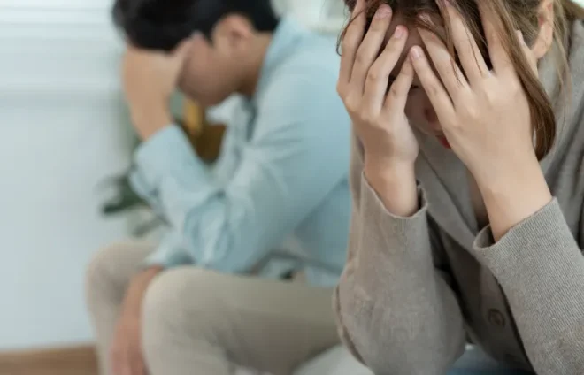 Upset couple sit apart, heads in hands, contemplating divorce and next steps at home tonight