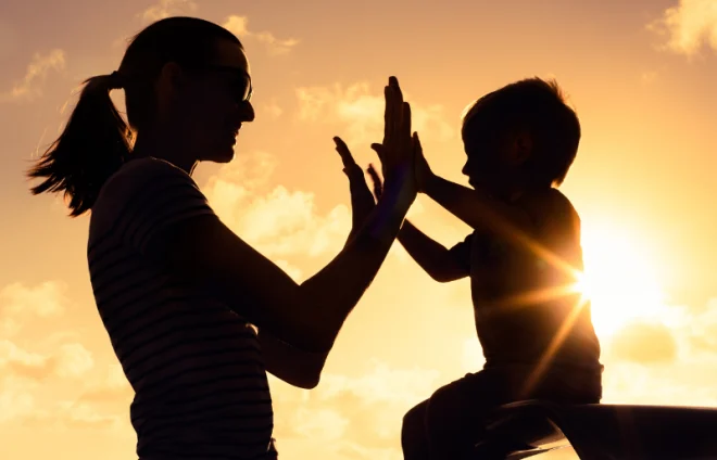 Silhouetted mother and child high five at sunset, symbolizing healing after divorce and change together