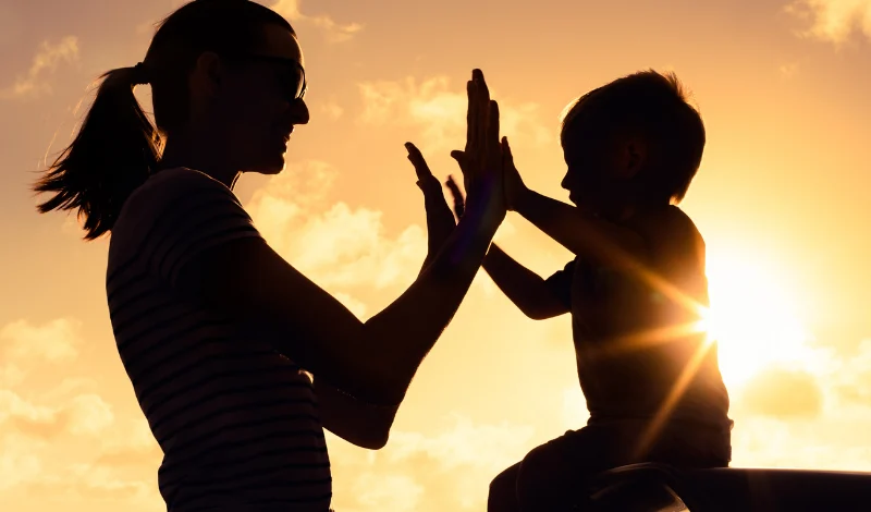 Silhouetted mother and child high five at sunset, symbolizing healing after divorce and change together