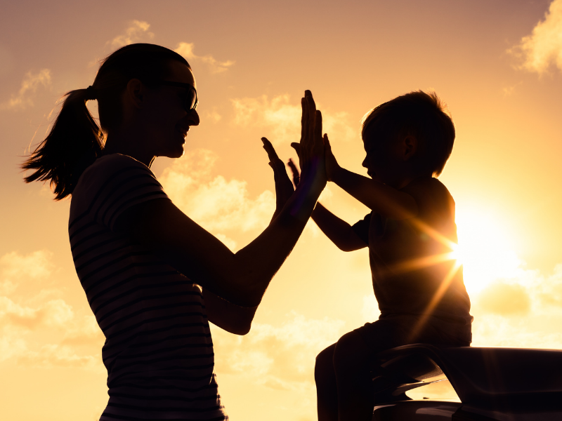 Silhouetted mother and child high five at sunset, symbolizing healing after divorce and change together