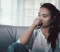 Woman sitting on a couch with her hand near her mouth, looking away in a quiet indoor setting