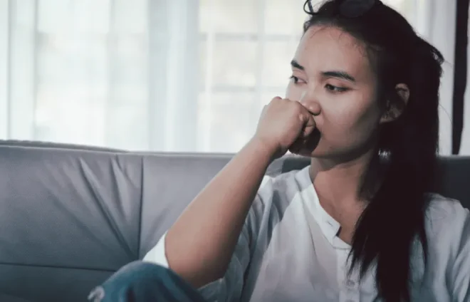 Woman sitting on a couch with her hand near her mouth, looking away in a quiet indoor setting