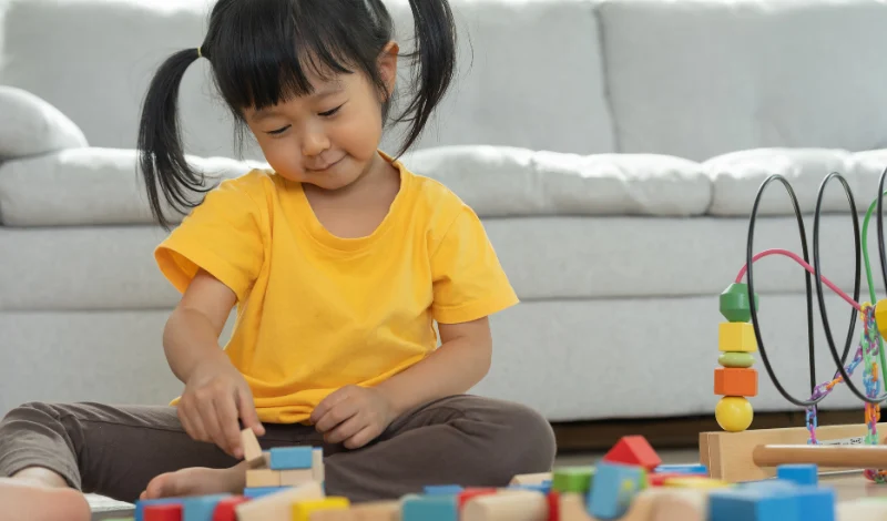 Young child builds wooden blocks on floor at home, focusing on shapes and colors independently