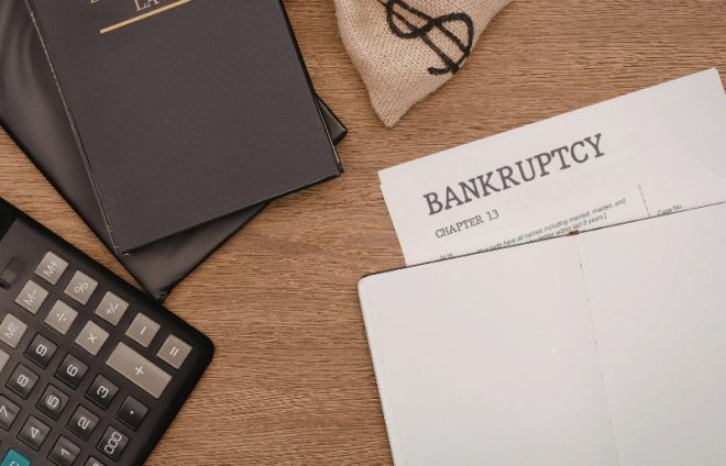 Bankruptcy document, calculator, money bag, and law book on desk, showing legal and financial stress