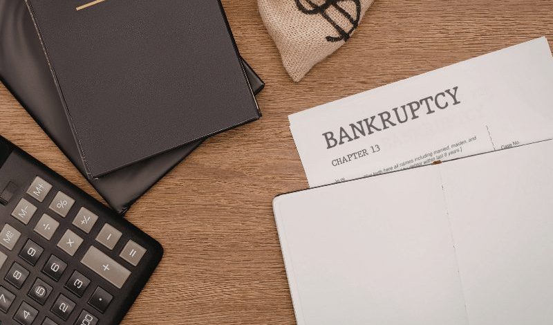 Bankruptcy document, calculator, money bag, and law book on desk, showing legal and financial stress