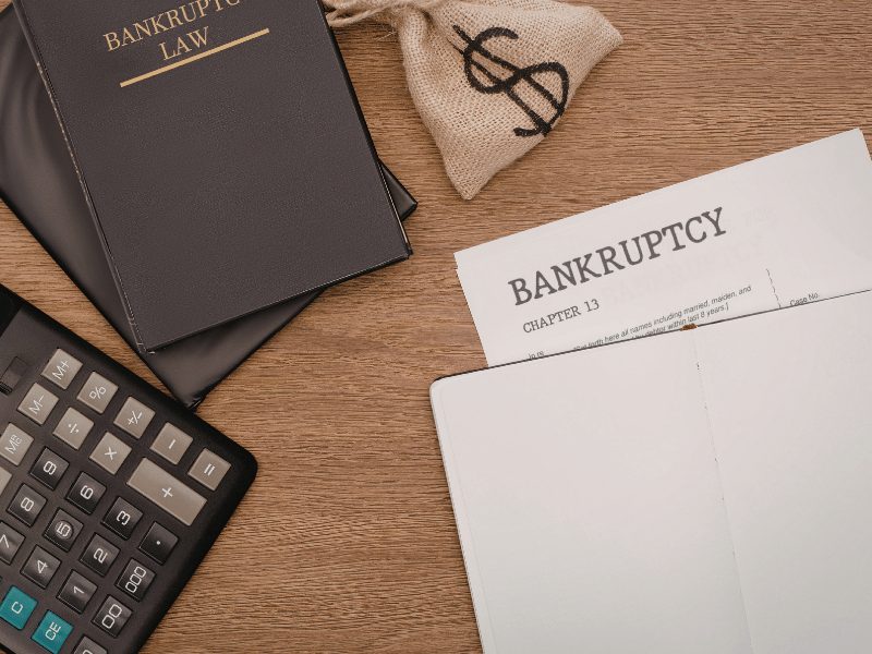 Bankruptcy document, calculator, money bag, and law book on desk, showing legal and financial stress