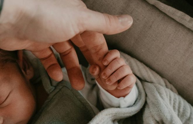 Newborn baby holding an adult finger, representing infant care, family ties, and parental responsibility