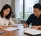 Divorce Agreement Signing An Asian couple sits across from each other at a wooden table, individually signing legal documents as part of their divorce proceedings in Singapore